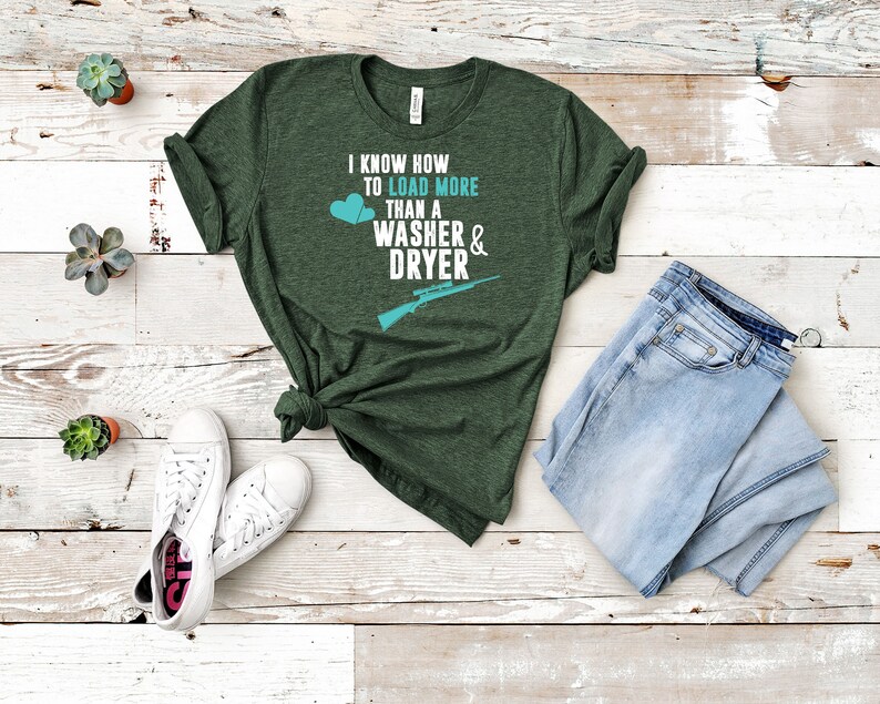 May include: A green t-shirt with the text "I know how to load more than a washer & dryer" and a rifle graphic. The shirt is laid out on a wooden surface with a pair of white sneakers and blue jeans.
