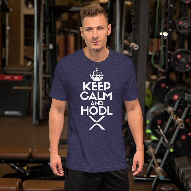 Puede incluir: Camiseta azul marino con el texto blanco "KEEP CALM AND HODL", coronada con un gr&aacute;fico de corona y el s&iacute;mbolo de la criptomoneda XRP. La camiseta de manga corta est&aacute; hecha de un material suave.