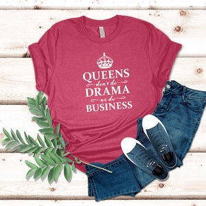 May include: A heathered dark pink short-sleeve t-shirt featuring a white graphic of a crown and the text "QUEENS don't do DRAMA we do BUSINESS" in a mix of serif and script fonts, paired with dark blue denim jeans and navy blue trainers.