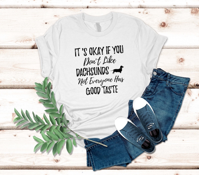 May include: White t-shirt with black text that reads "It's okay if you don't like dachshunds. Not everyone has good taste." A black silhouette of a dachshund is above the text.
