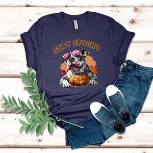 May include: A navy blue t-shirt with a white bulldog wearing pink sunglasses and holding a jack-o-lantern. The text "Stay Spooky" is printed in orange on the shirt.