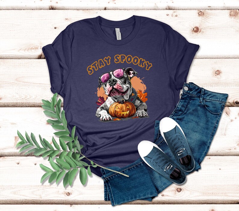 May include: A navy blue t-shirt with a white bulldog wearing pink sunglasses and holding a jack-o-lantern. The text "Stay Spooky" is printed in orange on the shirt.