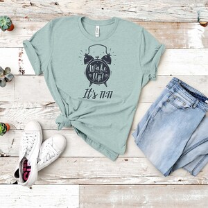 May include: A light blue t-shirt with a black alarm clock graphic and the text "Wake Up! It's 11:11".