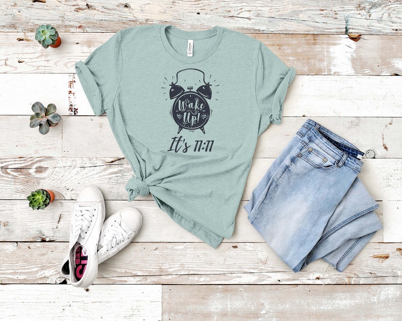 May include: A light blue t-shirt with a black alarm clock graphic and the text "Wake Up! It's 11:11".