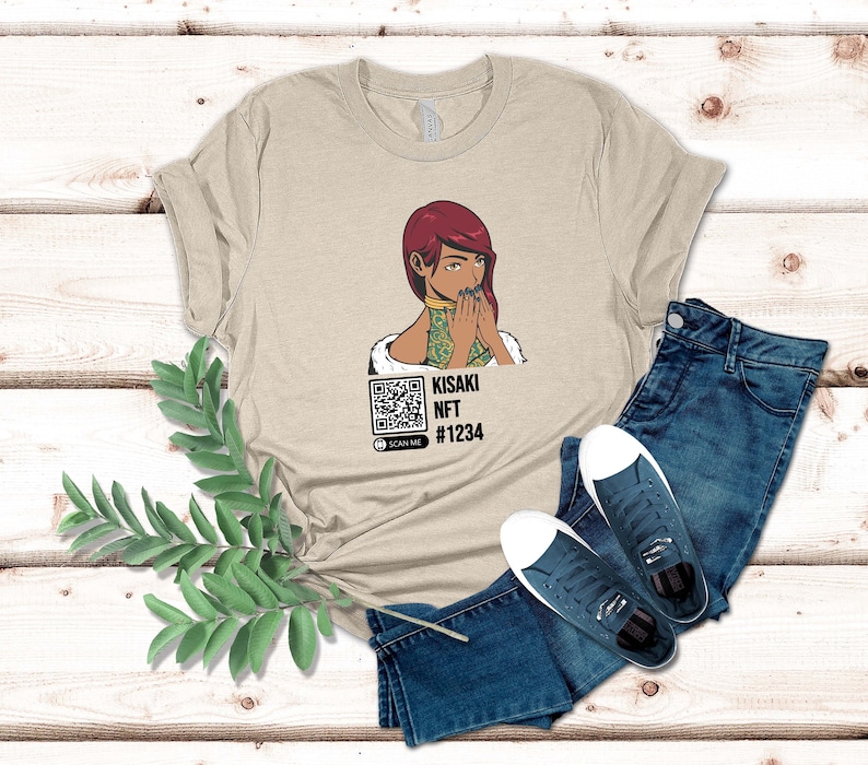 May include: Beige t-shirt featuring a graphic of a woman with red hair and a QR code. The text "KISAKI NFT #1234" is below the graphic. The shirt is paired with blue jeans and navy sneakers.