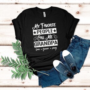 May include: Black t-shirt with white text that reads "My Favorite People Call Me Grandpa" with the names Evan, Gunnar, and Jenny underneath.