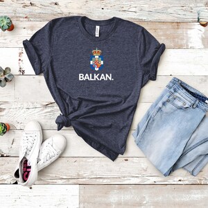 May include: A dark blue t-shirt with a white graphic of a coat of arms and the word "BALKAN."