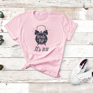 May include: Pink t-shirt with a black alarm clock graphic and the text "Wake Up! It's 11:11"