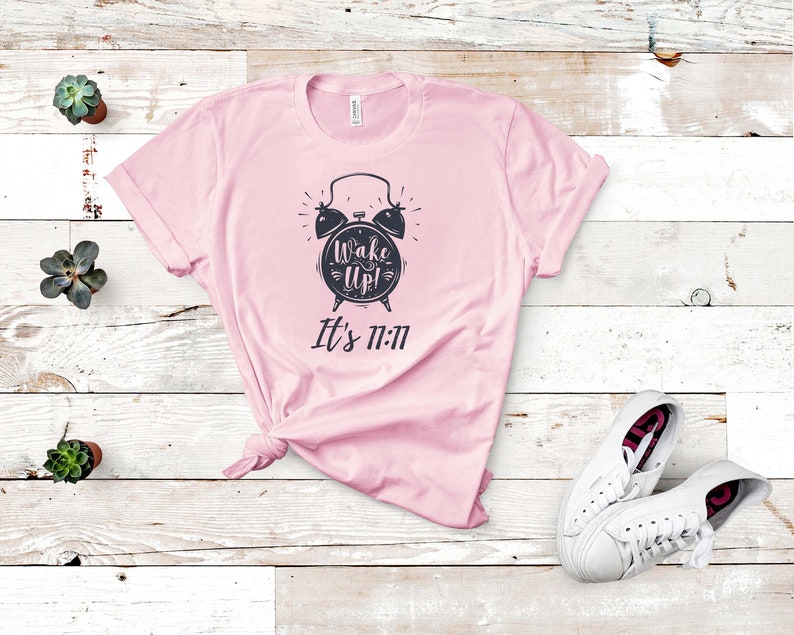 May include: Pink t-shirt with a black alarm clock graphic and the text "Wake Up! It's 11:11"