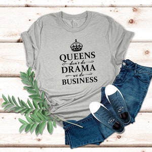May include: A heather grey short-sleeved t-shirt featuring a black crown graphic and the text QUEENS don't do DRAMA we do BUSINESS, paired with dark blue denim jeans and a pair of dark blue canvas trainers with white laces and rubber soles.