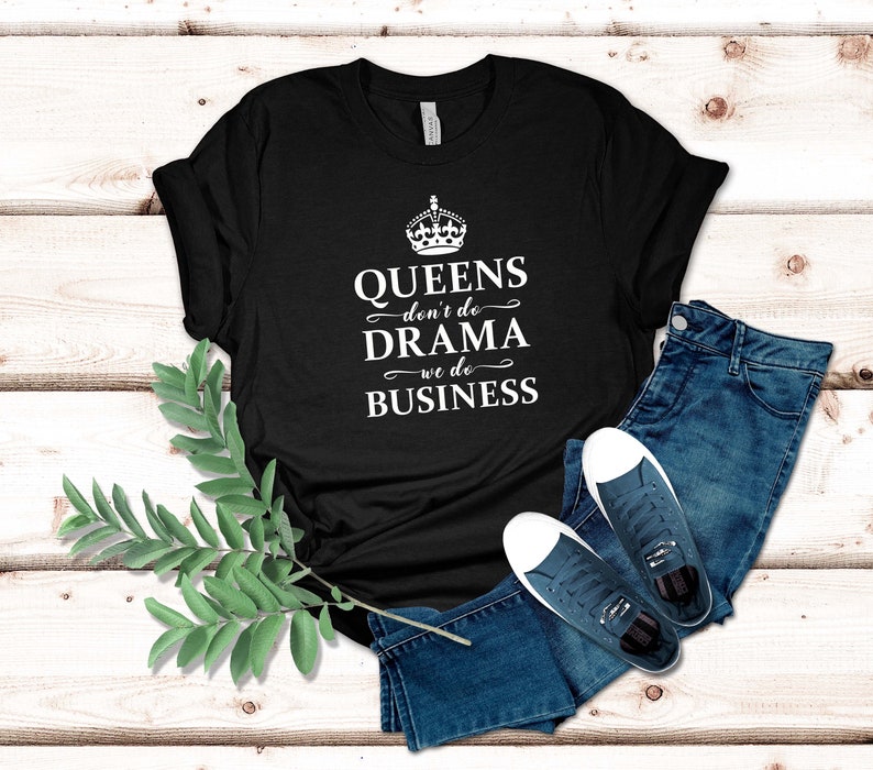 May include: A black short-sleeved t-shirt featuring a white graphic of a crown above the text "QUEENS don't do DRAMA we do BUSINESS". The shirt is paired with blue denim jeans and a pair of dark blue canvas trainers with white rubber soles.