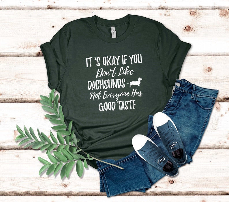 May include: A dark green t-shirt with white text that reads "It's okay if you don't like dachshunds. Not everyone has good taste." A white silhouette of a dachshund is next to the text.