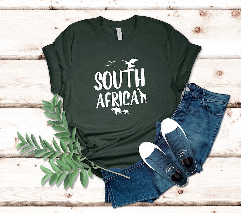 May include: Dark green t-shirt with the text "SOUTH AFRICA" in white, featuring silhouettes of an eagle, giraffe, and elephants. The shirt is paired with blue jeans and white-soled sneakers.