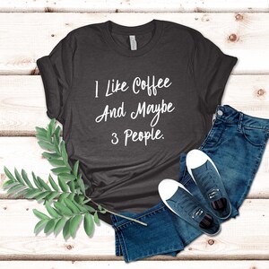 May include: A dark gray t-shirt with the text "I like coffee and maybe 3 people." printed in white.