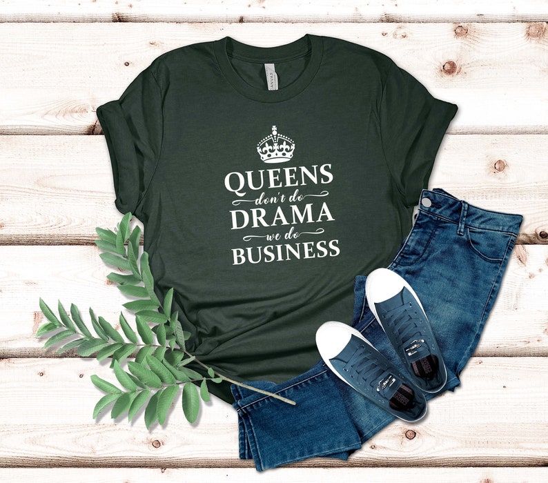 May include: A dark green short-sleeved t-shirt featuring a white graphic of a crown above the text "QUEENS don't do DRAMA we do BUSINESS," paired with blue denim jeans and a pair of dark blue canvas trainers with white laces and soles.