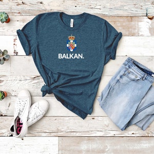 May include: A dark blue t-shirt with a white graphic of a coat of arms and the word "BALKAN."