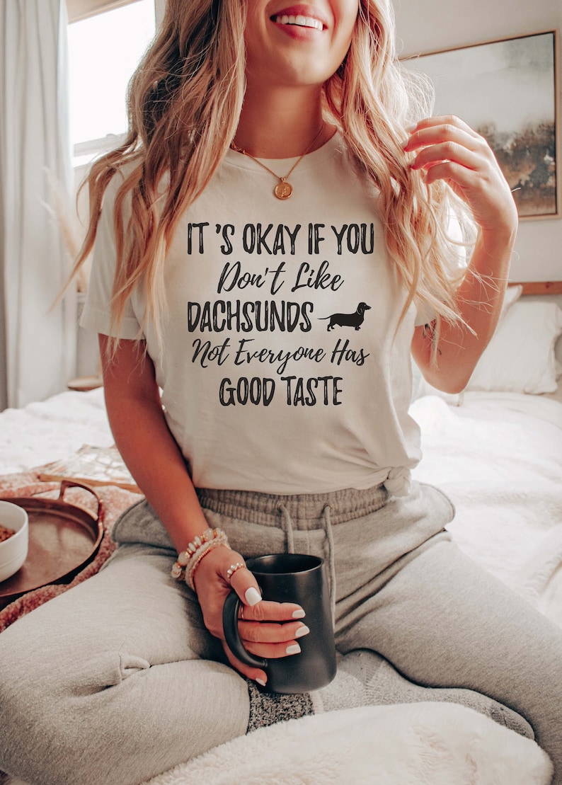 May include: White t-shirt with black text that reads "It's okay if you don't like dachshunds. Not everyone has good taste." A black dachshund silhouette is next to the word "dachshunds".