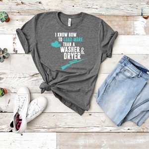 May include: A heather grey t-shirt with a teal graphic that says "I know how to load more than a washer & dryer" with a teal heart and a teal rifle graphic.