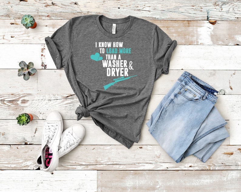 May include: A heather grey t-shirt with a teal graphic that says "I know how to load more than a washer & dryer" with a teal heart and a teal rifle graphic.