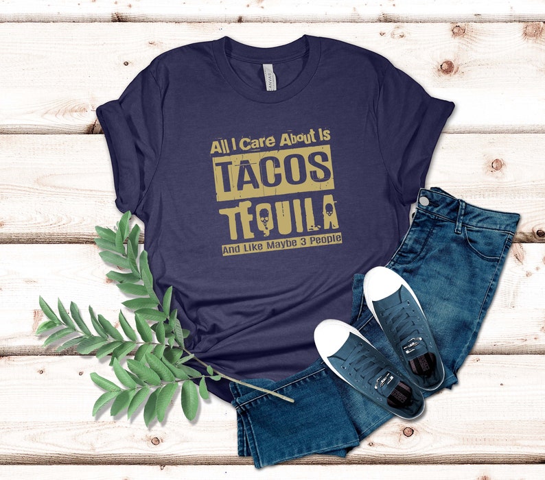 Pode incluir: Uma camiseta azul marinho com o texto "All I care about is tacos tequila and like maybe 3 people" em letras douradas.