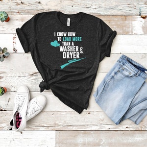 May include: A dark gray t-shirt with the text "I know how to load more than a washer & dryer" in white. Two blue hearts and a rifle graphic are also on the shirt.