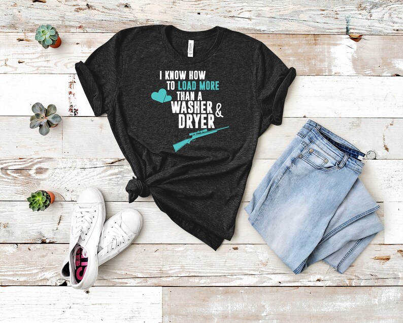May include: A dark gray t-shirt with the text "I know how to load more than a washer & dryer" in white. Two blue hearts and a rifle graphic are also on the shirt.