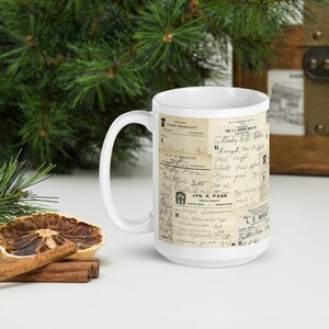 Op de afbeelding: Een witte keramische mok met een vintage ontwerp met een collage van oude handgeschreven recepten en apotheeklabels. De tekst bevat "Pages Pharmacy", "Baby 6.8 oz", "Mel. Srupt", "White Point Spe", "Sand", "Jas. E. Page" en "Le Muir".