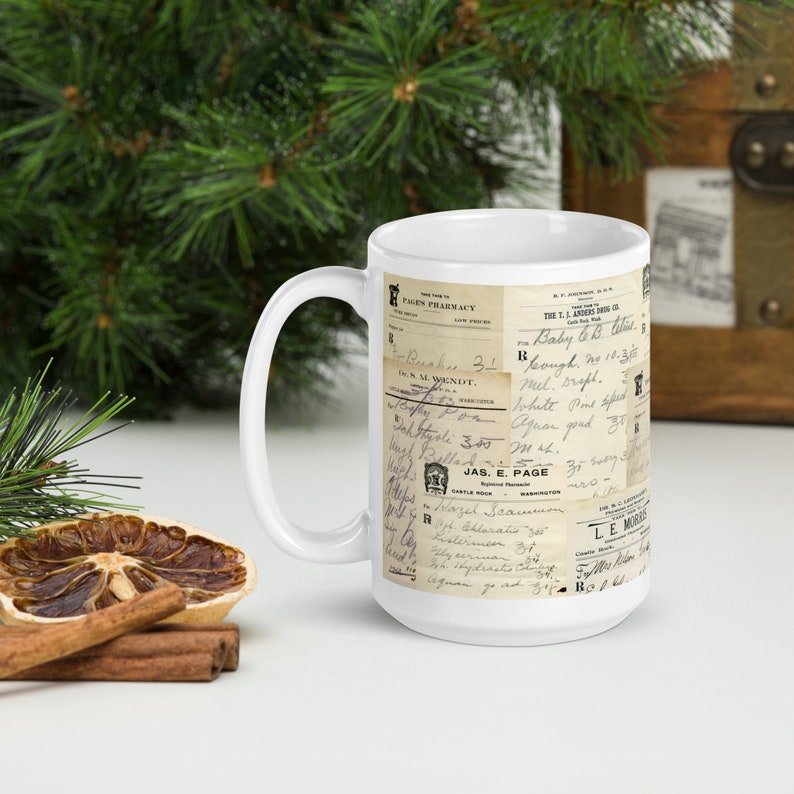 Op de afbeelding: Een witte keramische mok met een vintage ontwerp met een collage van oude handgeschreven recepten en apotheeklabels. De tekst bevat "Pages Pharmacy", "Baby 6.8 oz", "Mel. Srupt", "White Point Spe", "Sand", "Jas. E. Page" en "Le Muir".