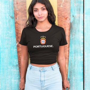 Może przedstawiać: Czarny t-shirt z białym napisem "PORTUGUESE". Koszulka posiada herb z koroną i kolorami czerwonym, ż&oacute;łtym i niebieskim. Modelka ma na sobie jasnoniebieskie szorty dżinsowe.