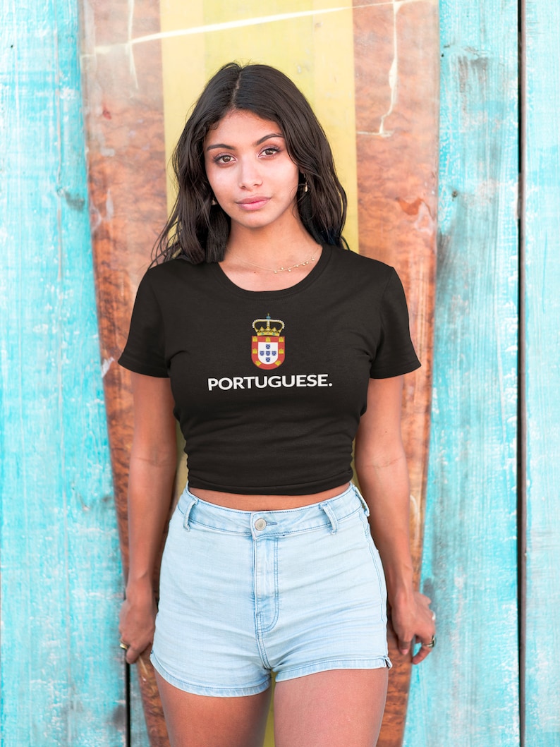 Może przedstawiać: Czarny t-shirt z białym napisem "PORTUGUESE". Koszulka posiada herb z koroną i kolorami czerwonym, ż&oacute;łtym i niebieskim. Modelka ma na sobie jasnoniebieskie szorty dżinsowe.