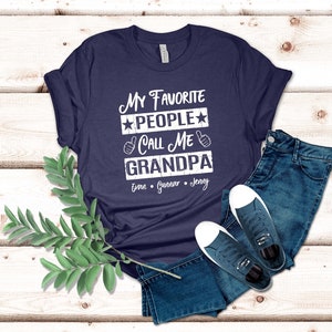 May include: Navy blue t-shirt with white text that reads "My Favorite People Call Me Grandpa" with three names listed below: Evan, Gunnar, Jenny.