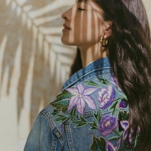 May include: A blue denim jacket with embroidered purple flowers on the back.