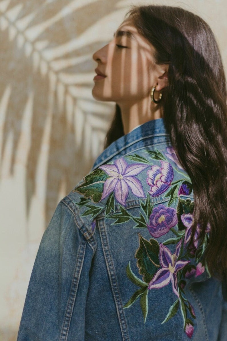 May include: A blue denim jacket with embroidered purple flowers on the back.