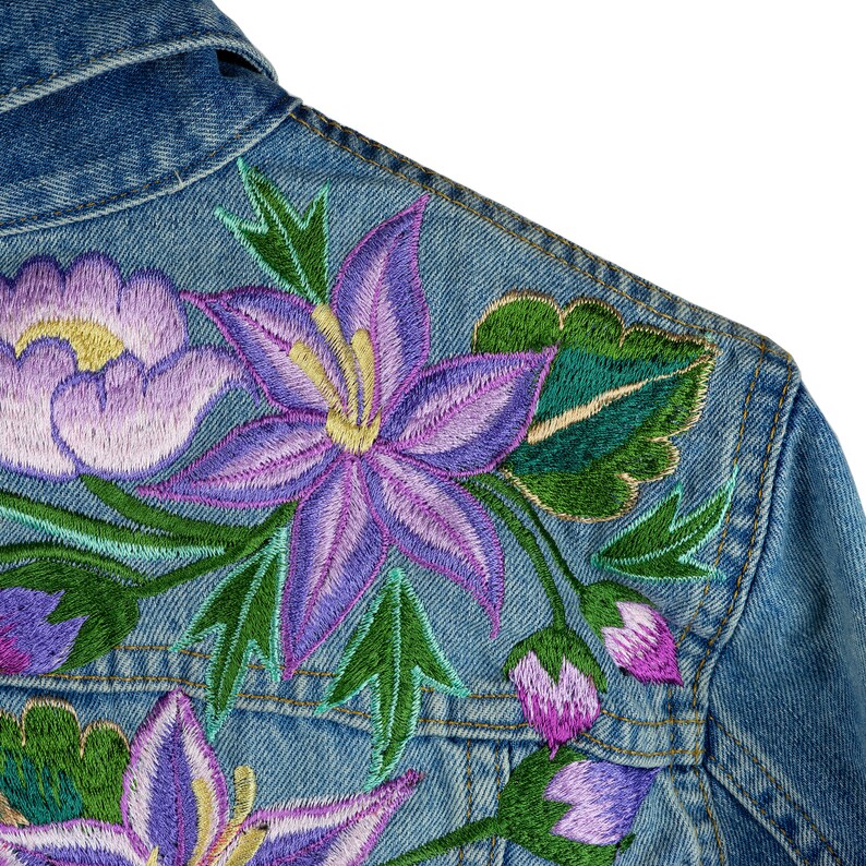 May include: A denim jacket featuring embroidered flowers in shades of purple, green, and yellow. The flowers are a mix of lilies and roses.