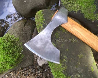 May include: A hand-forged axe with a wooden handle. The axe head is made of steel and has a curved blade. The axe is resting on a mossy rock.