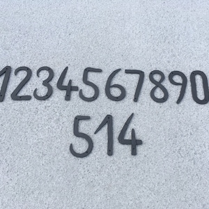 Könnte beinhalten: Schwarze Hausnummern aus Metall 1234567890 und 514. Die Zahlen sind an einer hellgrauen, strukturierten Oberfläche befestigt.