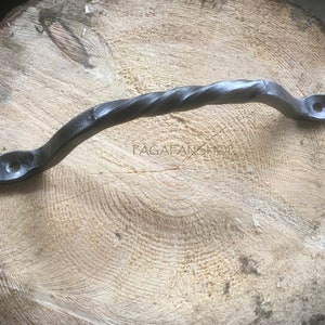 Puede incluir: Una manija de puerta de metal negro retorcida con forma redondeada. La manija está hecha de hierro forjado y tiene un aspecto rústico.