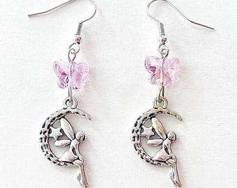 May include: Silver earrings with a crescent moon charm featuring a fairy sitting on it. The moon charm has a star design. The earrings are topped with a pink butterfly charm.