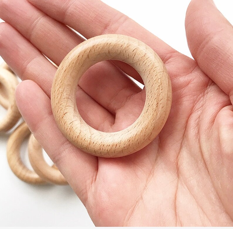 May include: A set of five unfinished wooden rings, ideal for crafting or DIY projects. The rings are smooth and have a natural wood colour.