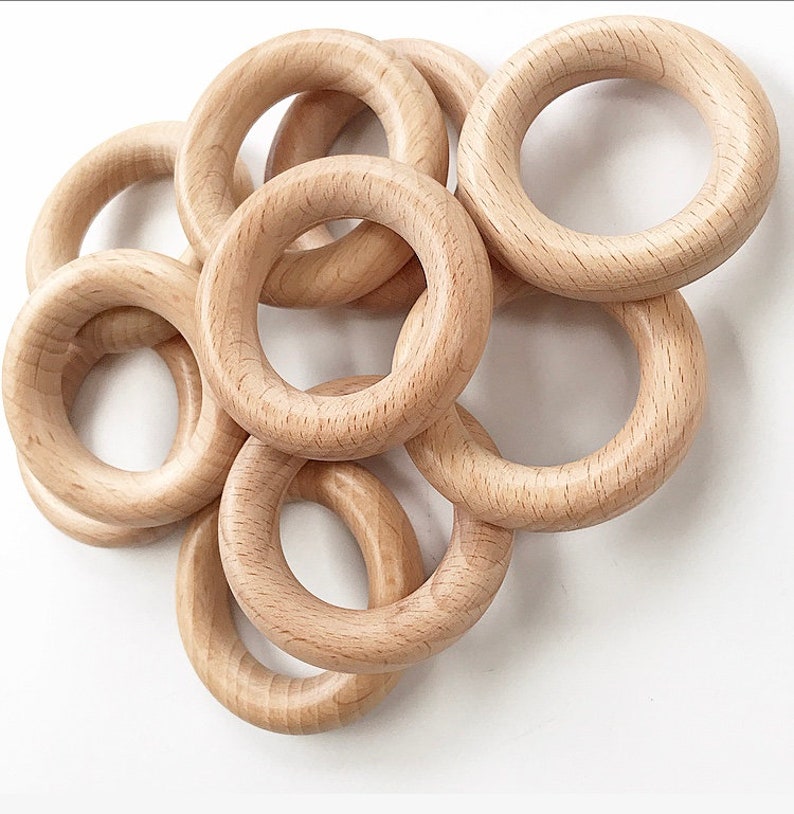 May include: A set of six natural wood rings, each with a smooth, unfinished surface. The rings are of varying sizes and are stacked together in a loose pile.