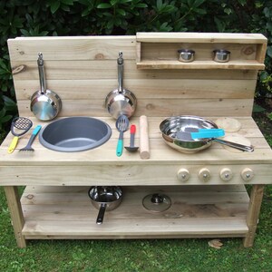 May include: Wooden play kitchen with a sink, hob, and shelves. It includes a variety of play kitchen accessories, such as pots, pans, utensils, and a rolling pin.