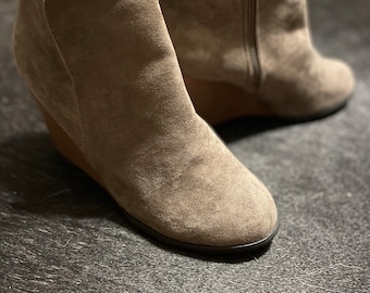 May include: A pair of gray suede ankle boots with a wedge heel. The boots have a zipper on the side and a pointed toe.