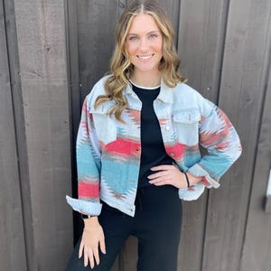 May include: A light blue denim jacket with a red, white, and blue geometric pattern. The jacket has a button closure and long sleeves.