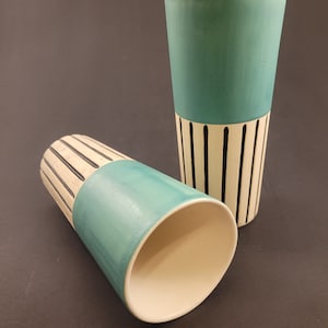May include: Two ceramic cups with a teal and white striped design. The cups are tall and cylindrical.