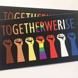 May include: Two black rectangular prints with the words "TOGETHER WE RISE" in colorful letters. Below the text are seven raised fists in various skin tones and colors, including brown, yellow, red, white, and blue.