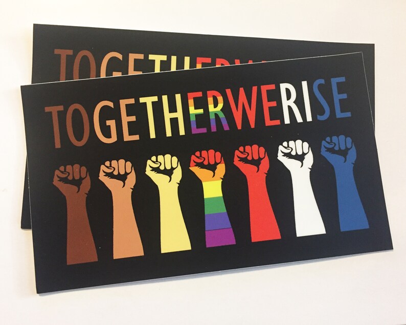 May include: Two black rectangular prints with the words "TOGETHER WE RISE" in colorful letters. Below the text are seven raised fists in various skin tones and colors, including brown, yellow, red, white, and blue.