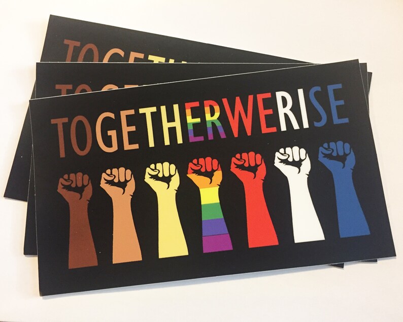 May include: Black rectangular cards with the words "TOGETHER WE RISE" in colorful letters. Below the text are seven raised fists in various skin tones and colors, including a rainbow-colored fist. The cards are stacked.
