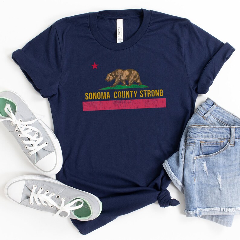 May include: A navy blue t-shirt with a distressed California flag design featuring a red star, a brown bear, and the text "Sonoma County Strong".