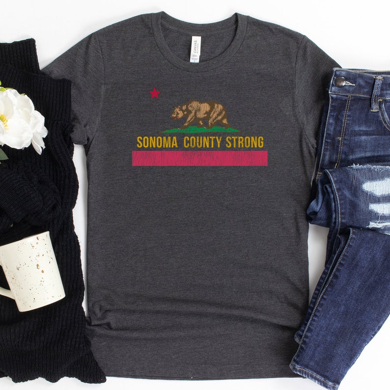 May include: A dark heather grey t-shirt with a distressed graphic of the California state flag featuring a bear and the text "Sonoma County Strong".