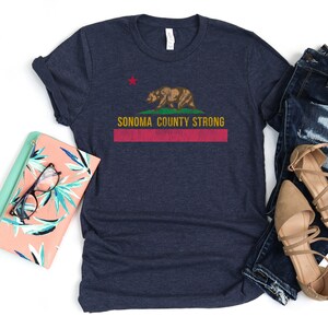 May include: A navy blue t-shirt with a distressed red, white, and yellow graphic of the California state flag with a bear and the text "Sonoma County Strong".